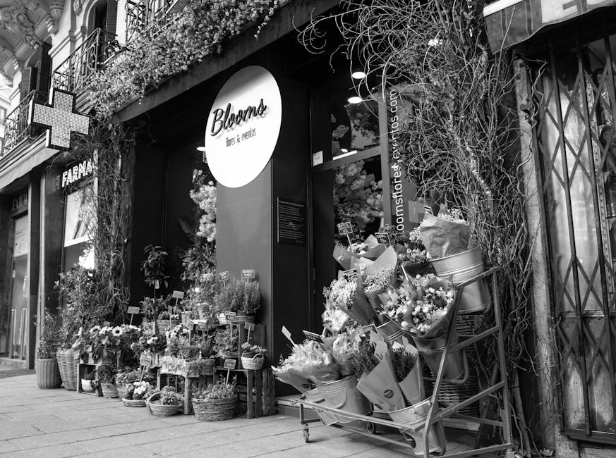A floral shop storefront with a sign reading 'Blooms flowers & gifts', showcasing an array of fresh flower arrangements outside. The display includes bouquets wrapped in paper, featuring various flowe