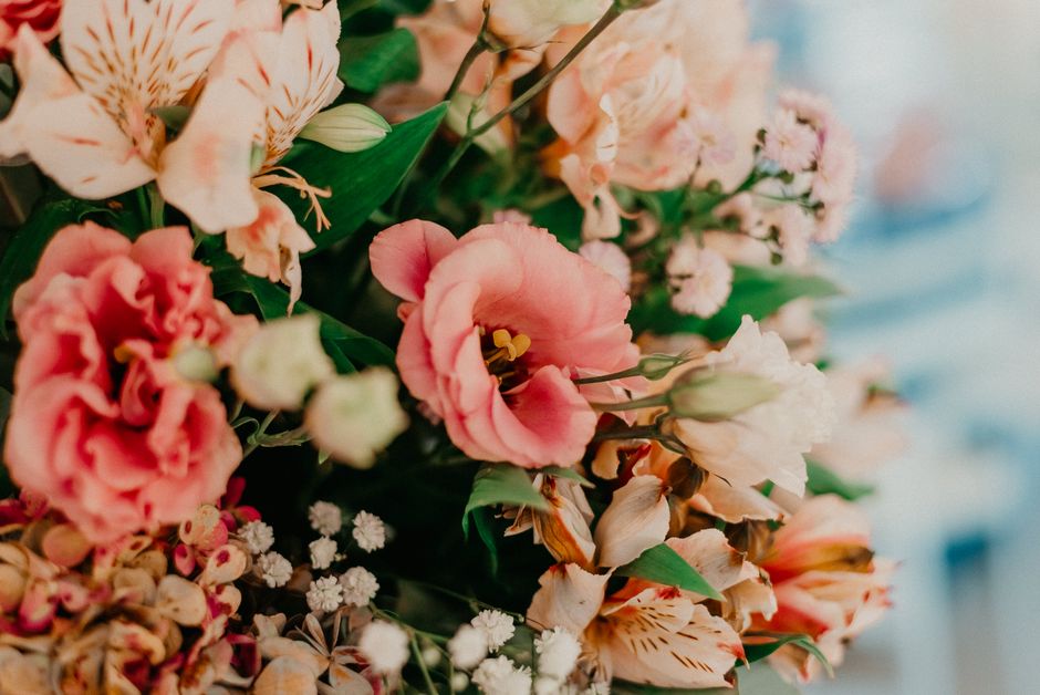 A vibrant floral arrangement featuring a variety of fresh flowers including pink lisianthus, peach and cream alstroemeria, and small white baby's breath, arranged with lush green foliage. The flowers 